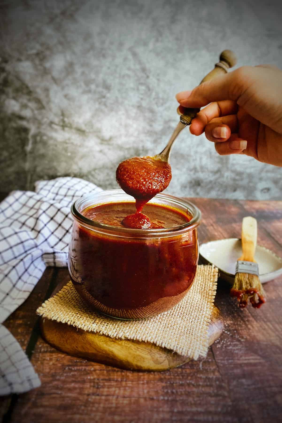 Vegan BBQ sauce in a jar with hand holding up a spoonful.