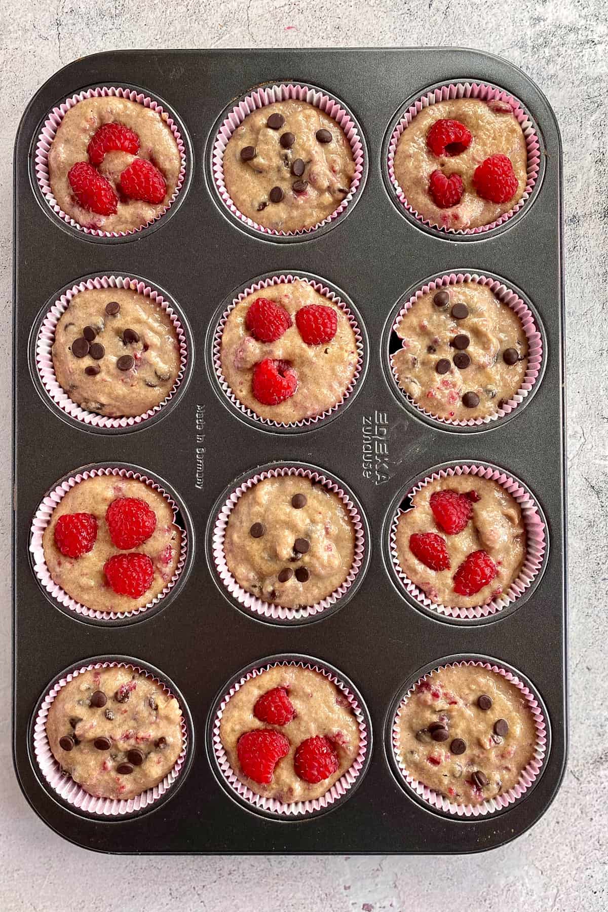 Uncooked vegan raspberry (and raspberry chocolate chip) muffins in a tin.