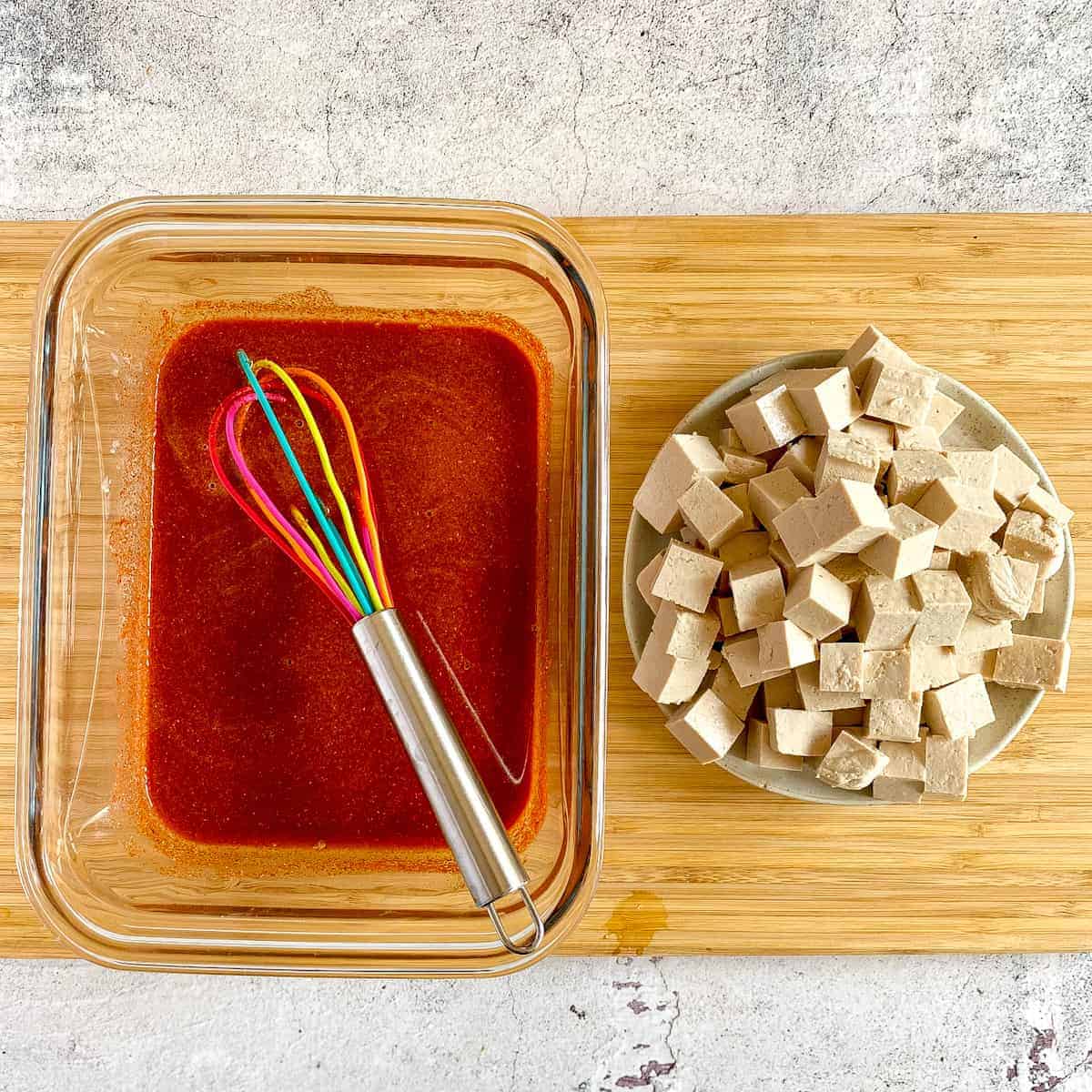 Tofu marinade and cubed tofu on a cutting board.