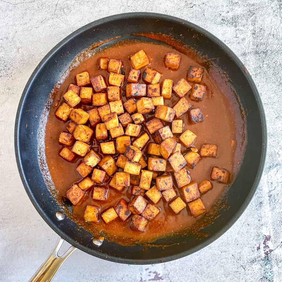 Marinated tofu in skillet with sauce.
