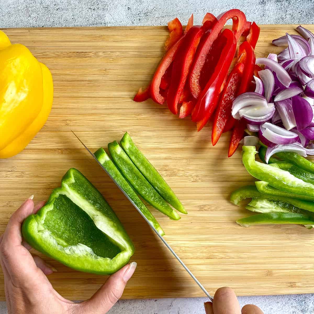 Hands chopping peppers and onions for fajita veggies.