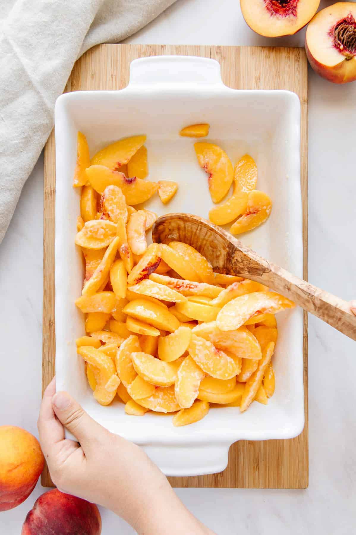 Hand mixing peaches in a dish.
