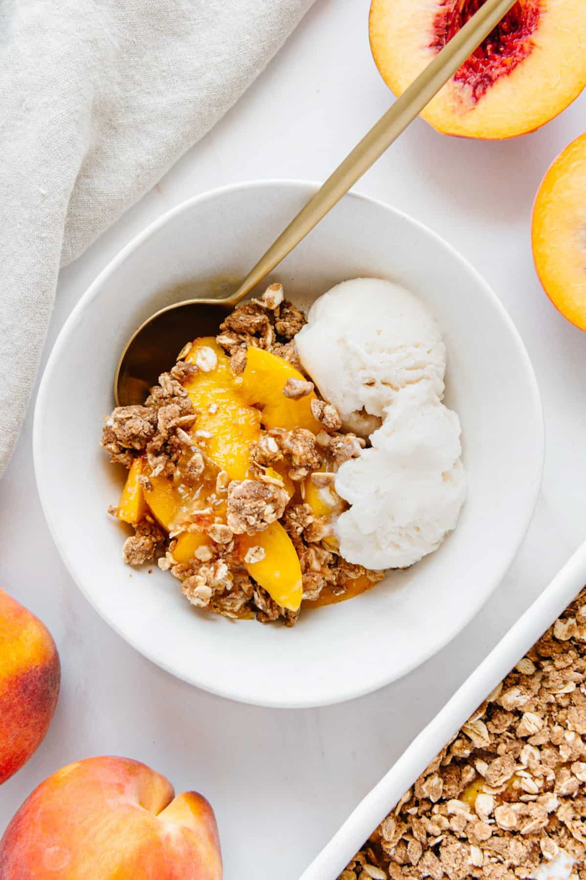 Vegan peach crumble in a bowl with vanilla ice cream.