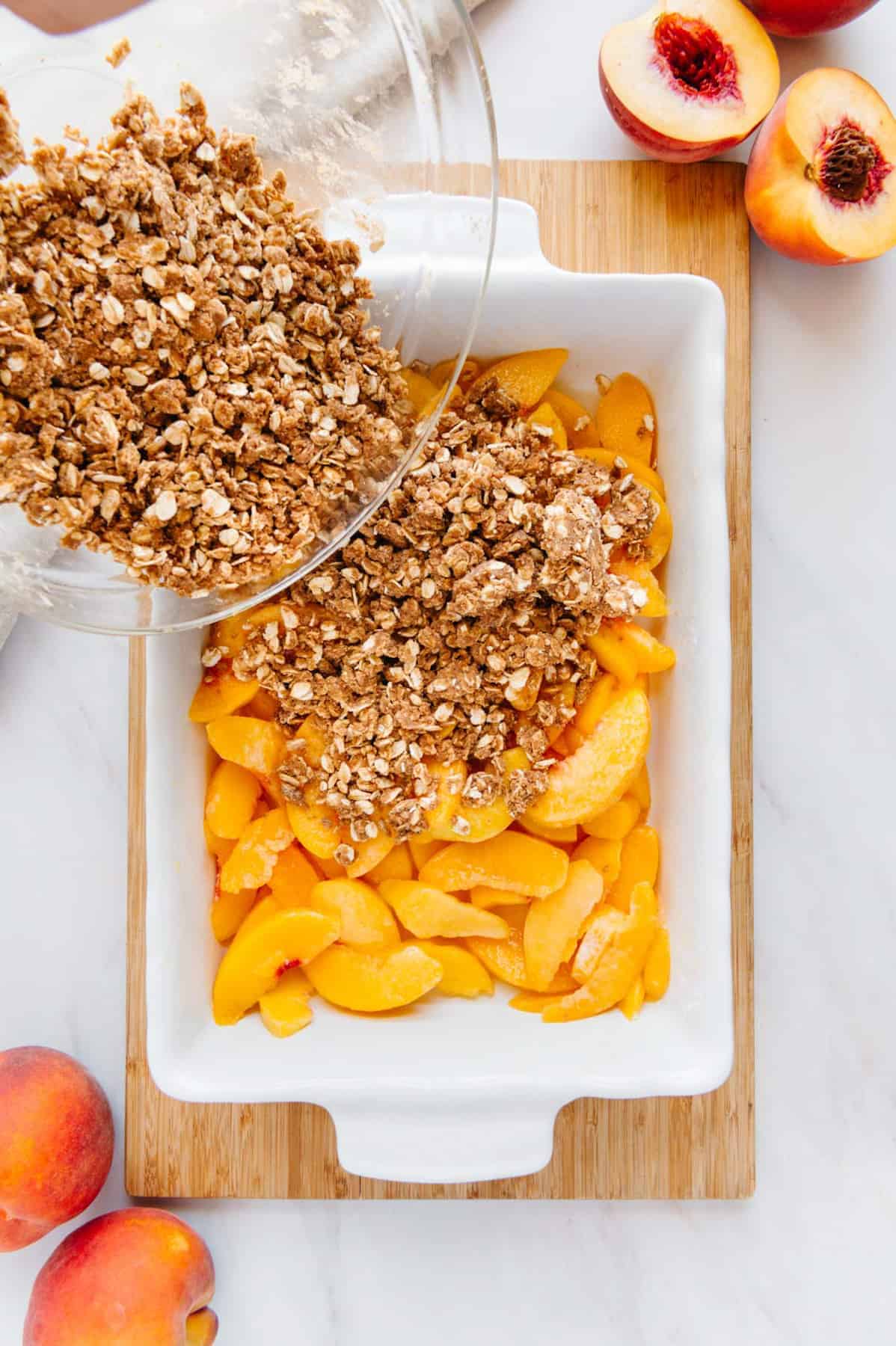 Bowl of crumble topping being dumped onto the peaches.