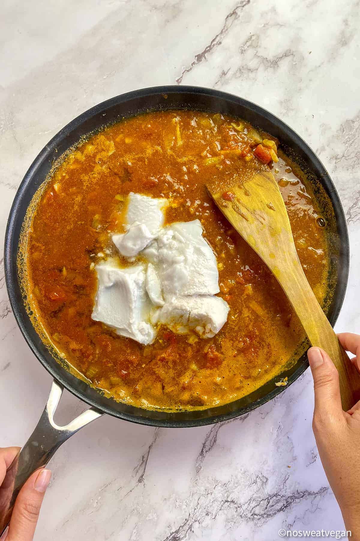 Coconut milk added to curry in a skillet.