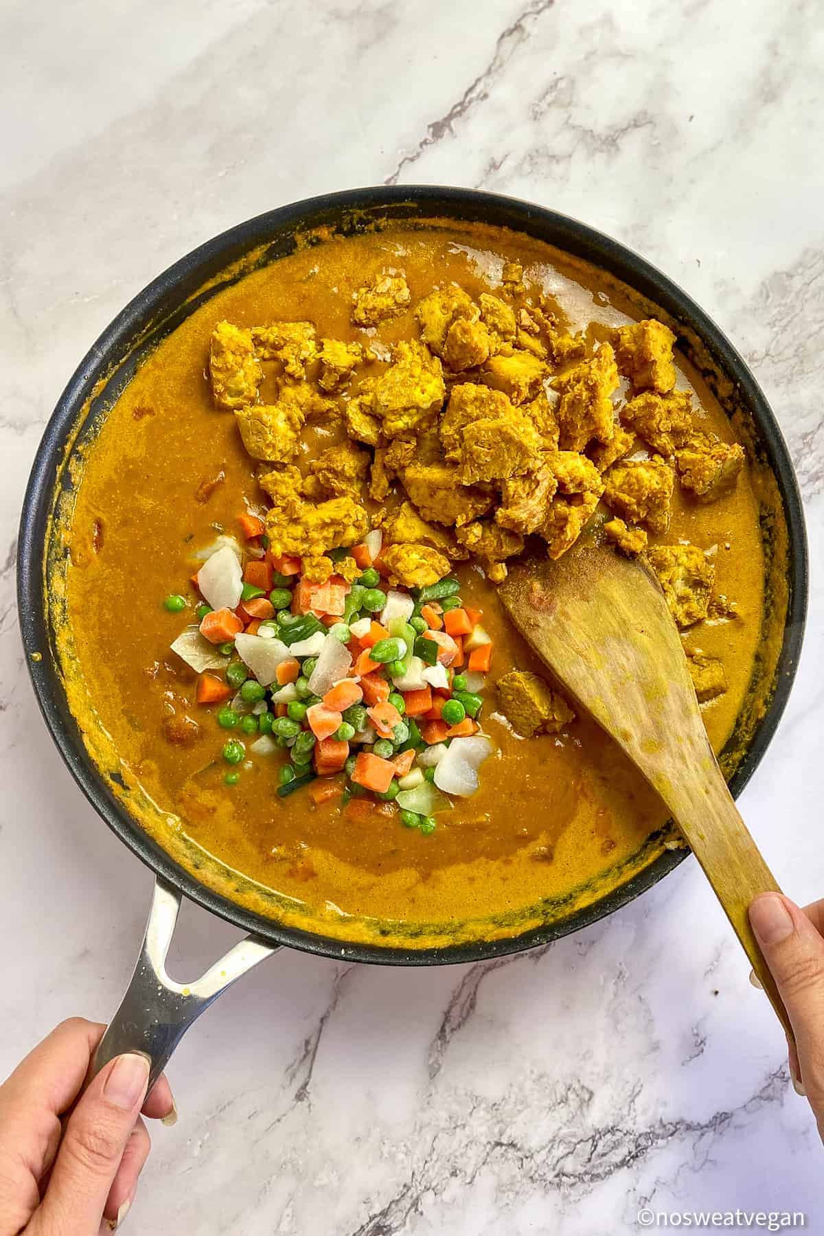 Tofu and mixed frozen vegetables added to curry in a skillet.