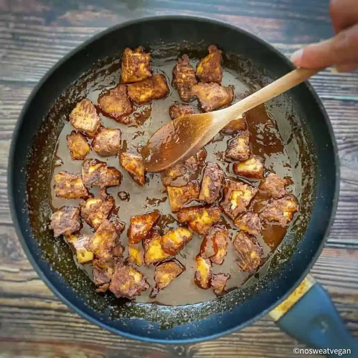 Hand mixing orange tofu in a skillet.