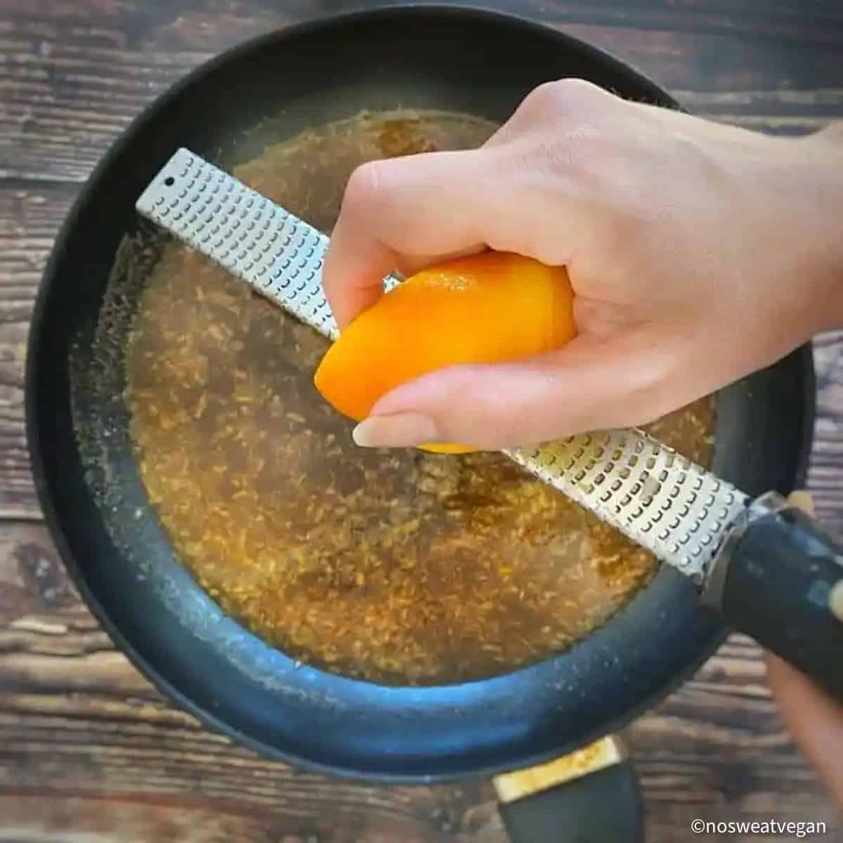 Hand grating orange peel into orange tofu sauce.