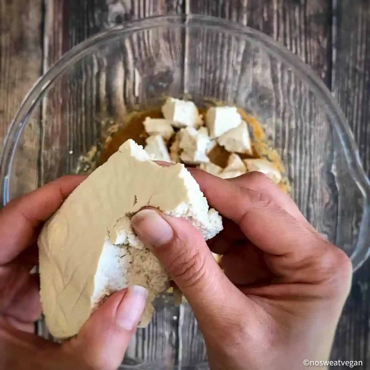 Hands breaking a block of tofu into chunks.