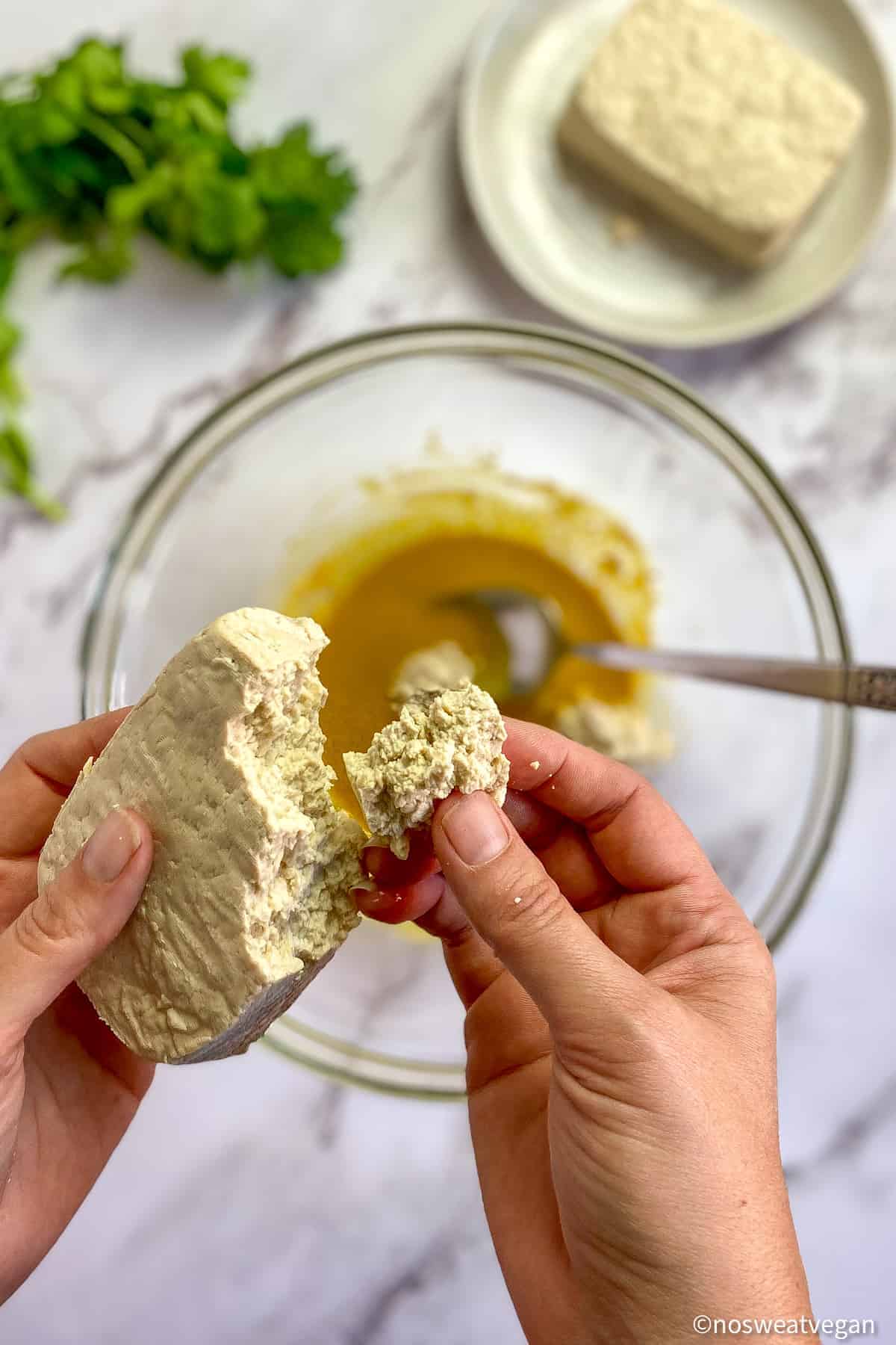 Hands breaking tofu into chunks over a bowl.