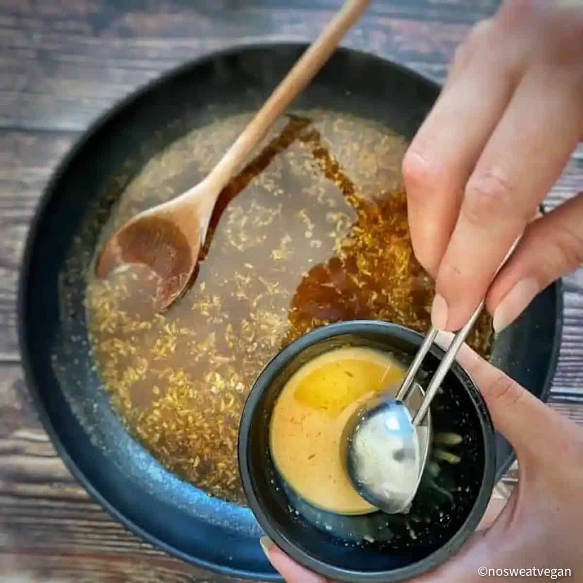 Orange tofu sauce with hand holding a small bowl with tempered cornstarch.