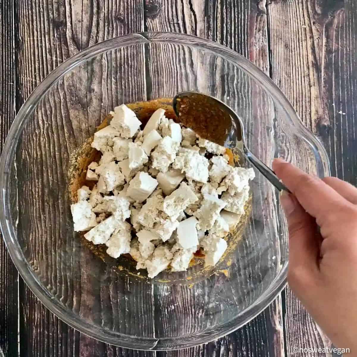 Tofu chunks in bowl with hand mixing them with the paste.