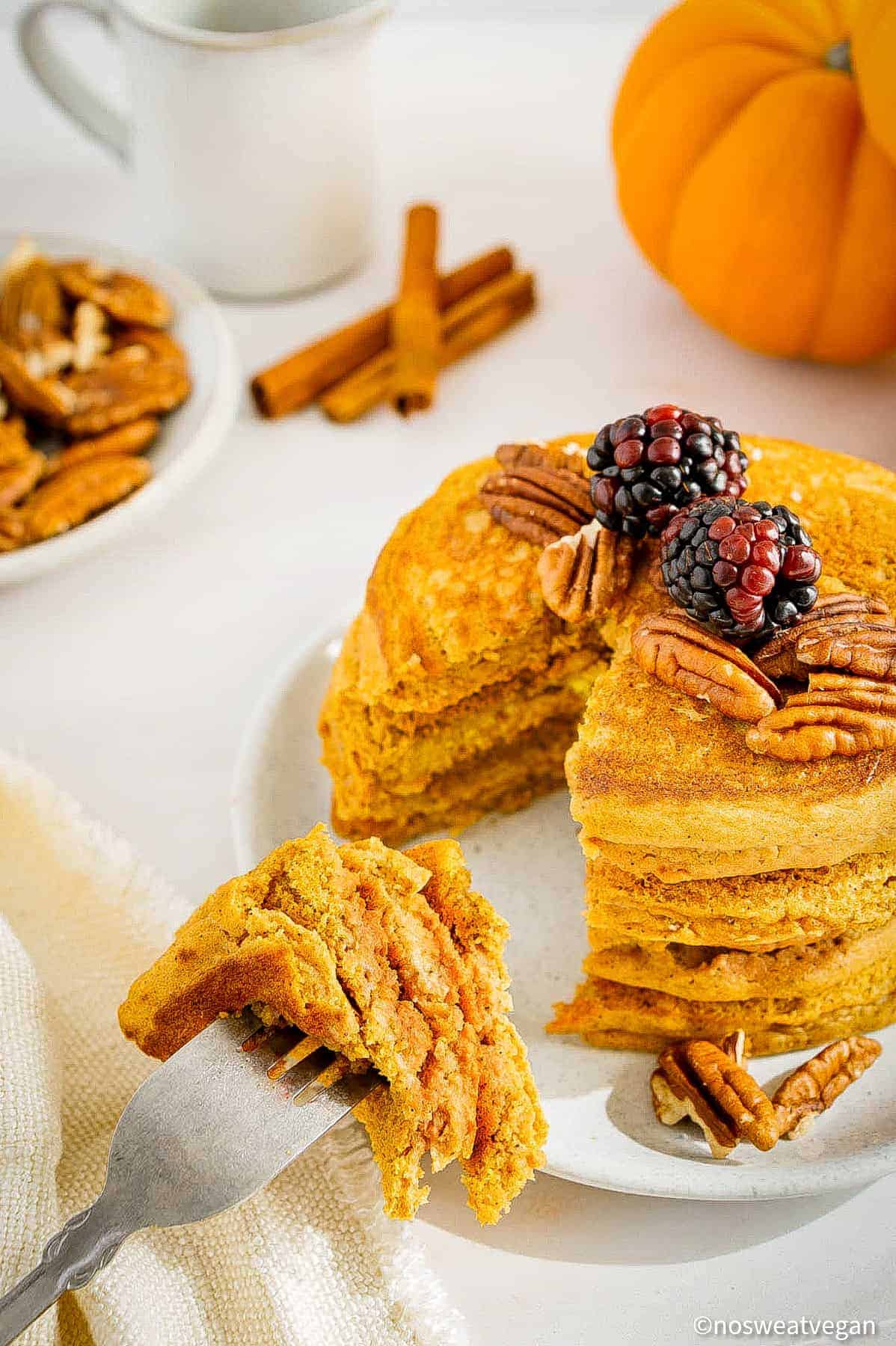 Vegan pumpkin pancakes stacked on a plate with a fork holding a bite of pancakes.