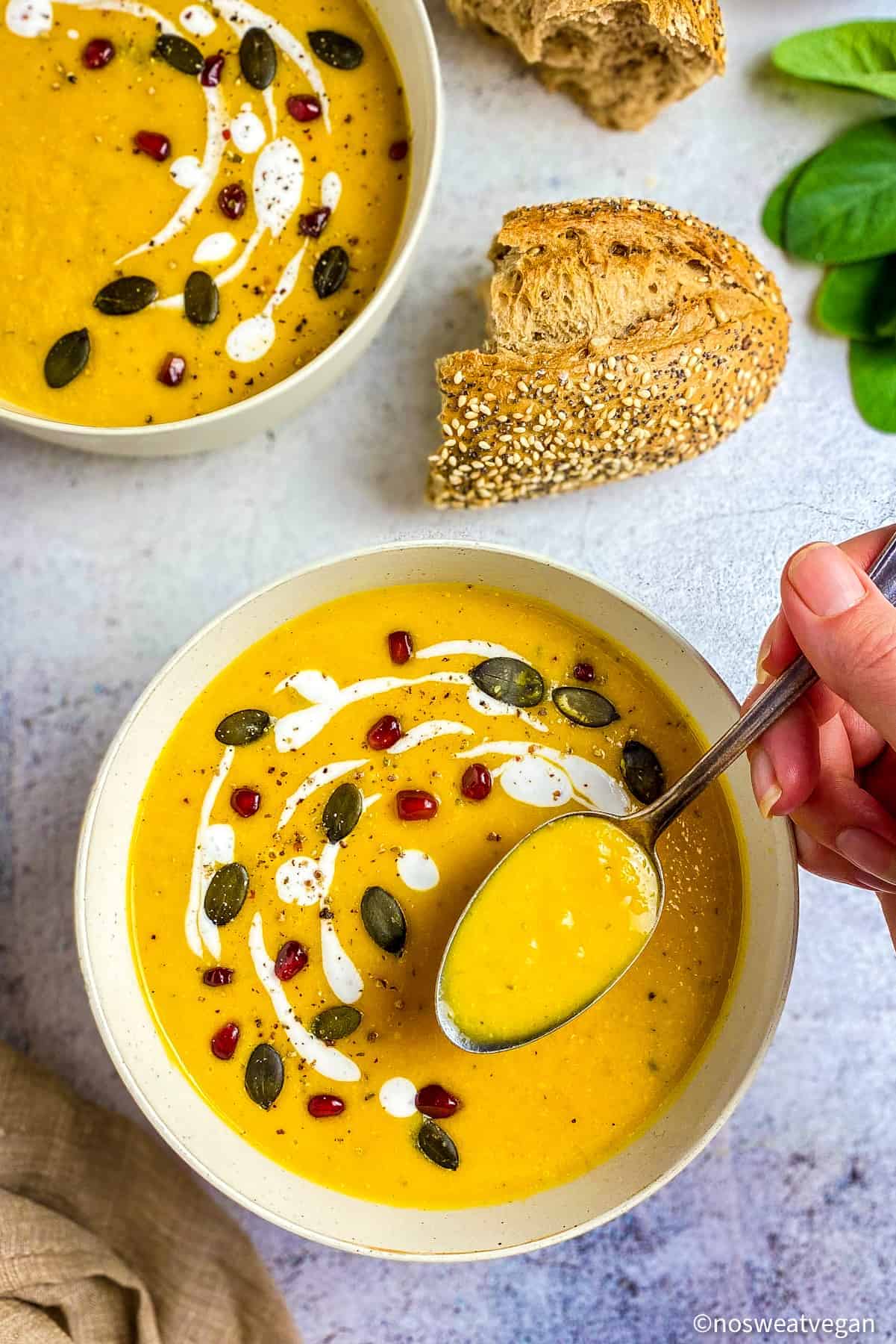 Butternut squash soup in a bowl with a hand lifting up a spoonful.