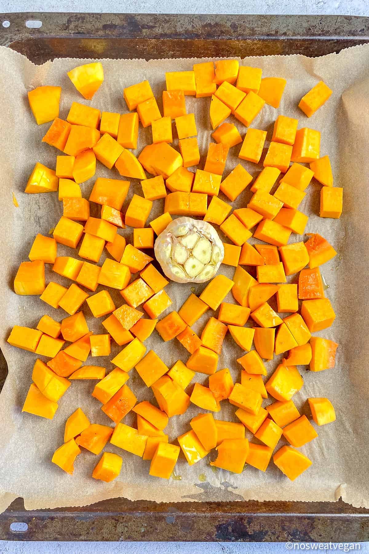 Butternut squash and garlic on a sheet pan.