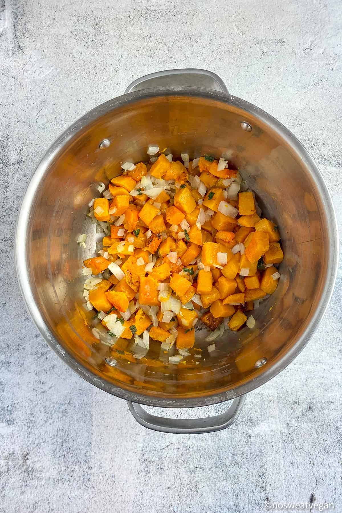 Roasted butternut squash in soup pot with onions and sage.