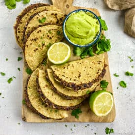 Vegan black bean tacos on a cutting board with avocado crema and limes.