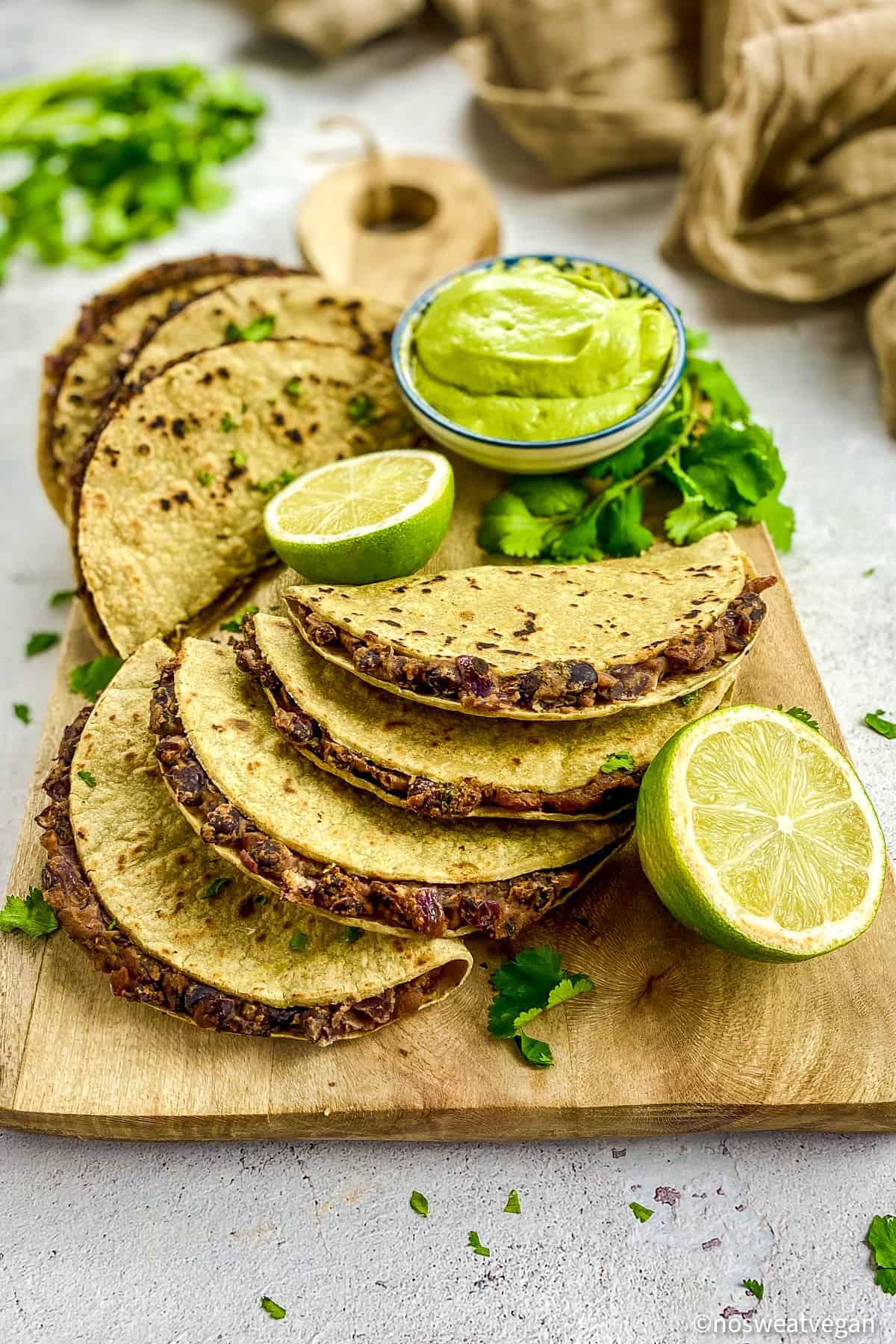 Black bean tacos on a cutting board with limes and avocado crema.