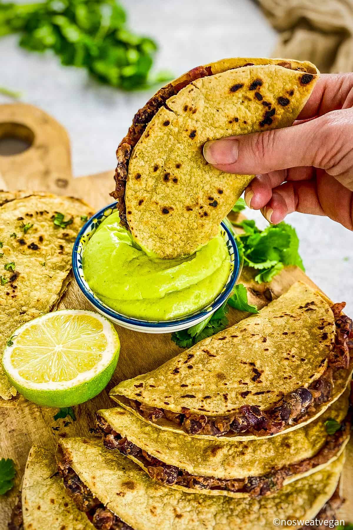 Hand dipping a black bean taco into avocado crema.