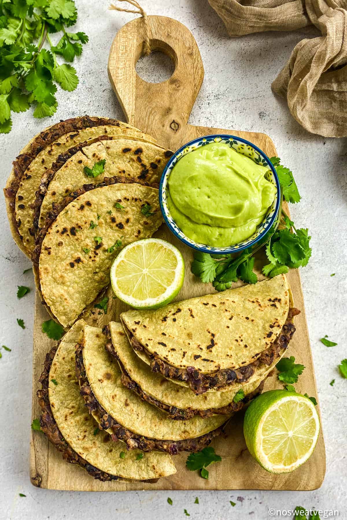 Vegan black bean tacos on a cutting board with avocado crema and limes.