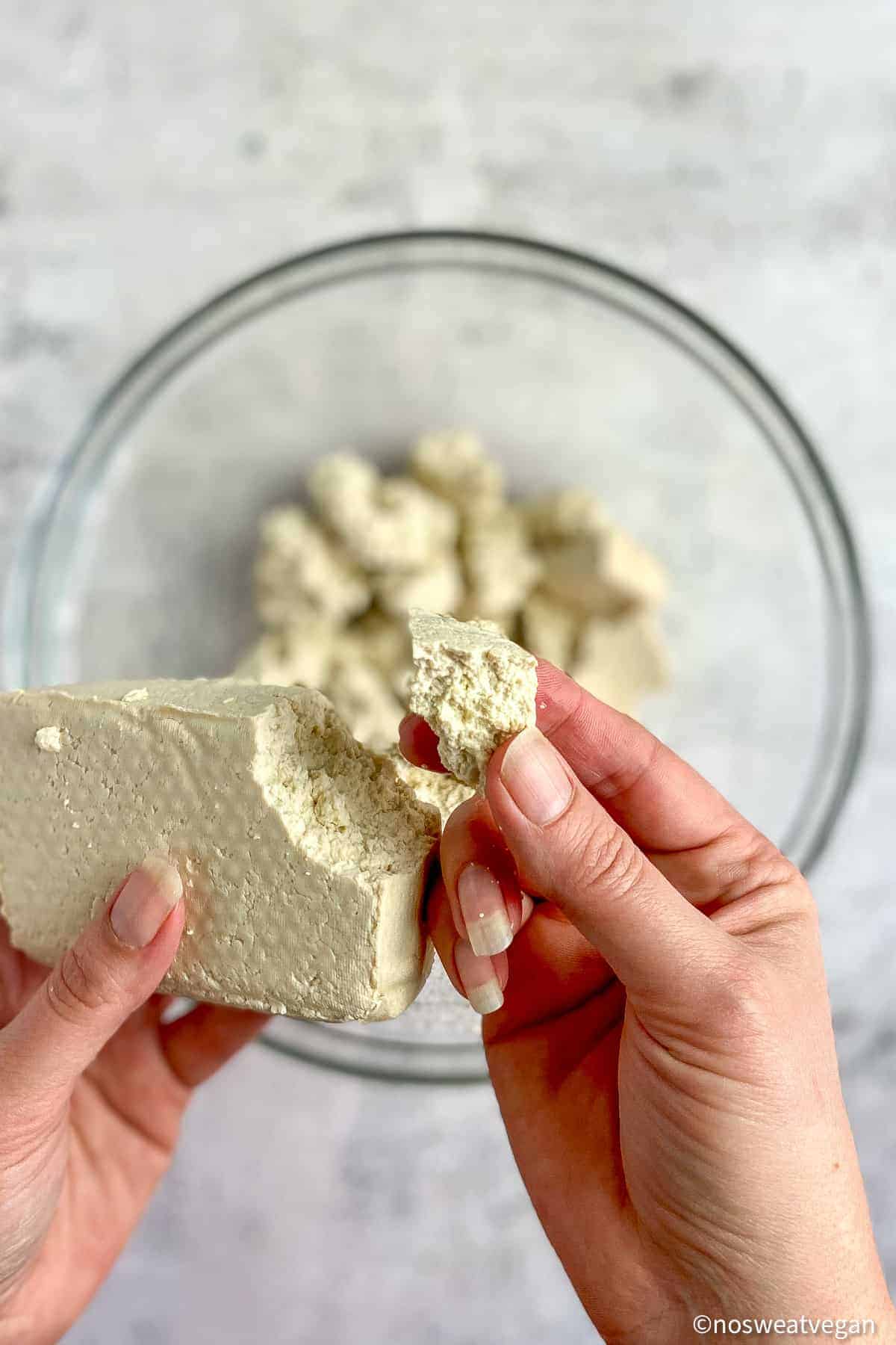 Hand breaking off a chunk from a block of tofu.