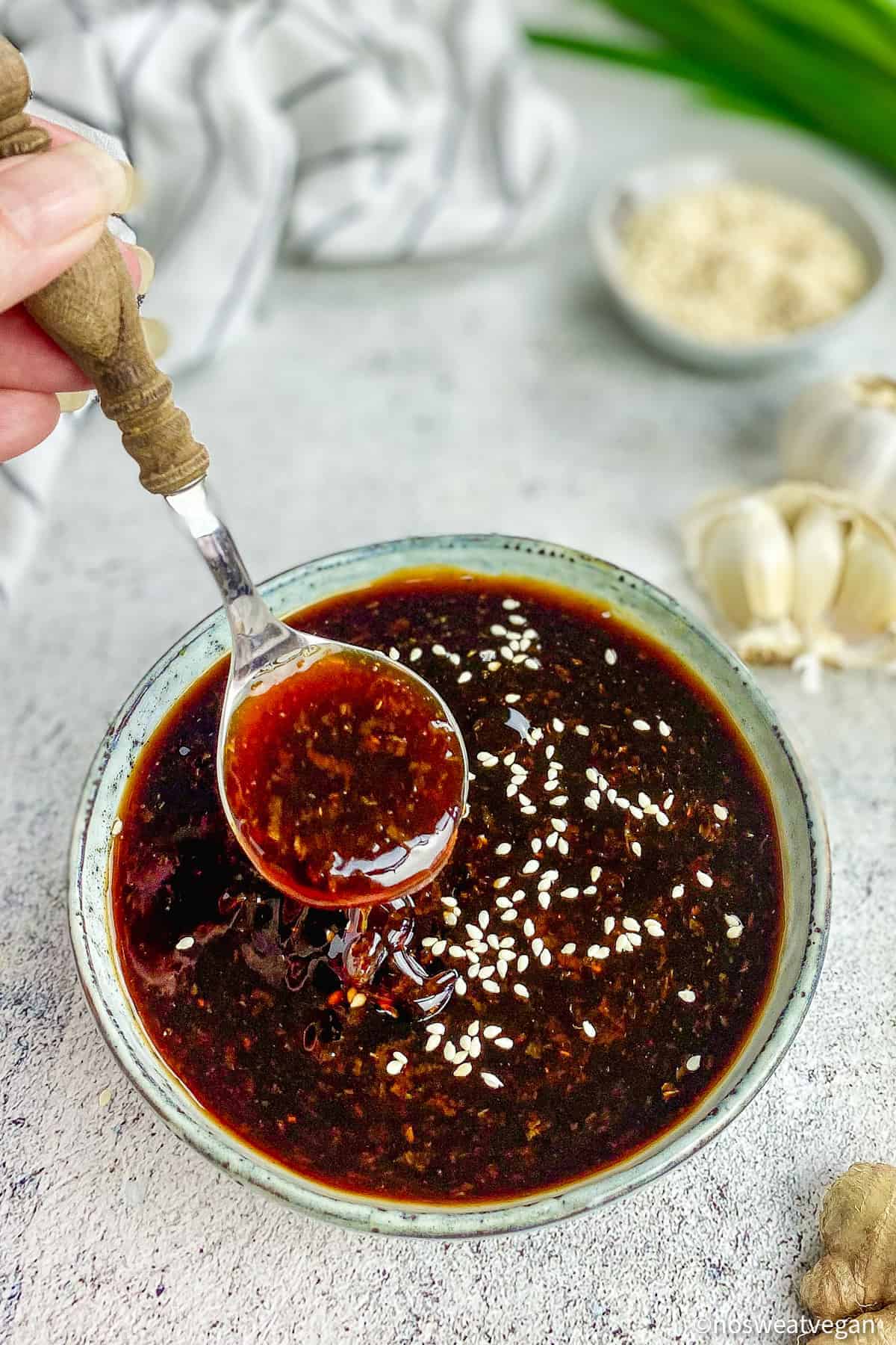 Hand lifting a spoonful of vegan teriyaki sauce from a bowl.