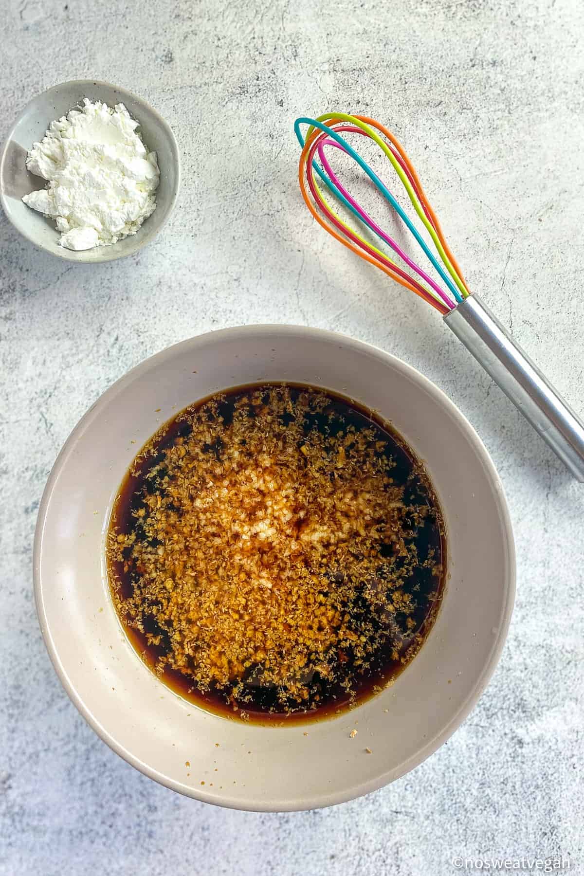 Vegan teriyaki sauce in a bowl next to a whisk and a small bowl of cornstarch.