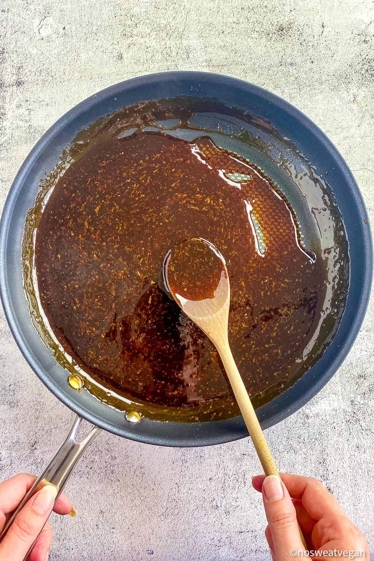 Teriyaki sauce in a skillet with a hand holding a wooden spoon.