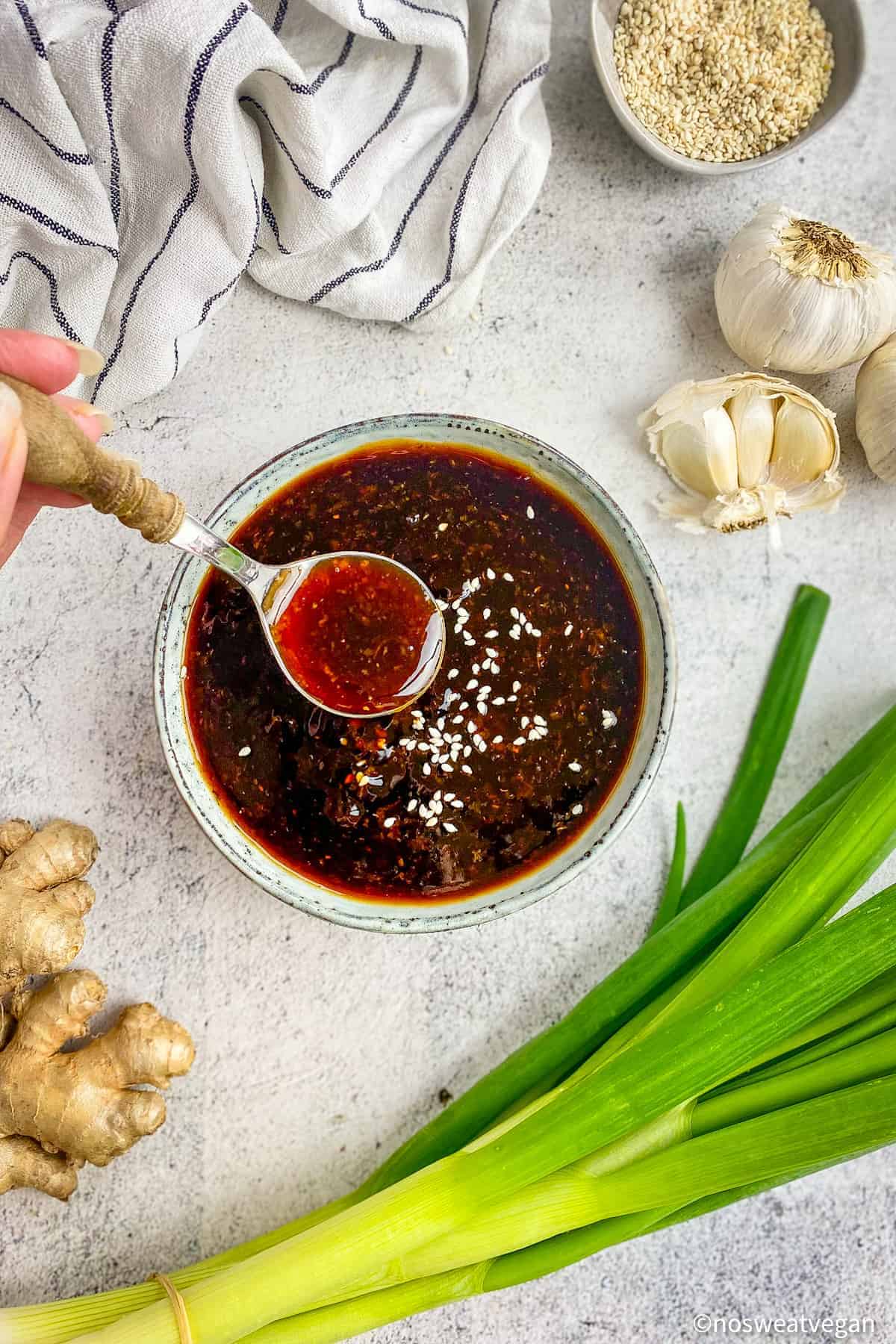 Vegan teriyaki sauce in a bowl with a hand lifting a spoon out.