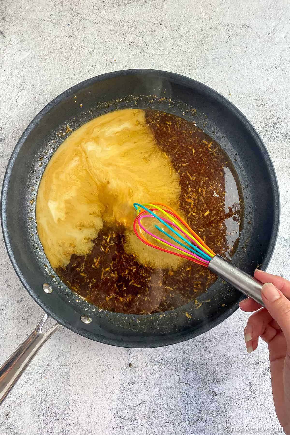 Skillet with teriyaki sauce and cornstarch slurry with hand whisking.