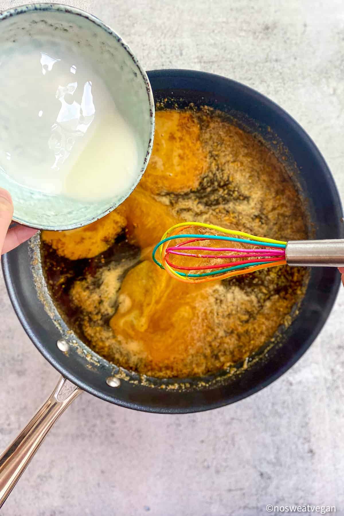 Hand hold bowl of cornstarch slurry as it is whisked into the teriyaki sauce.