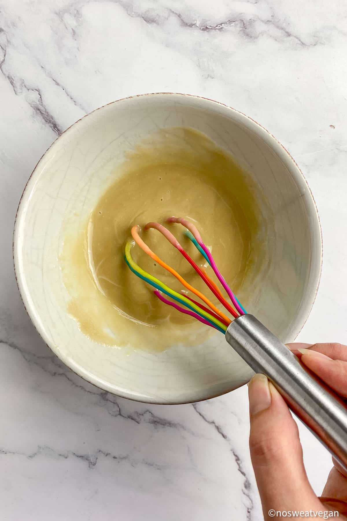 Hand whisking a bowl of creamy apple cider vinegar dressing.