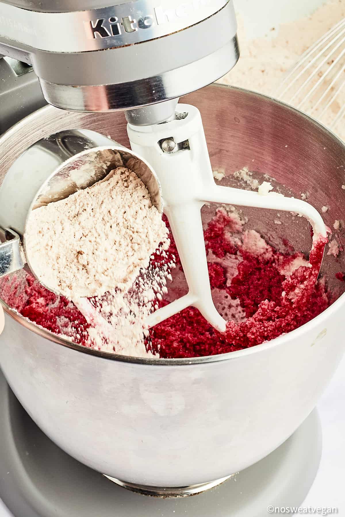 Measuring cup adding flour to red velvet cookie dough.