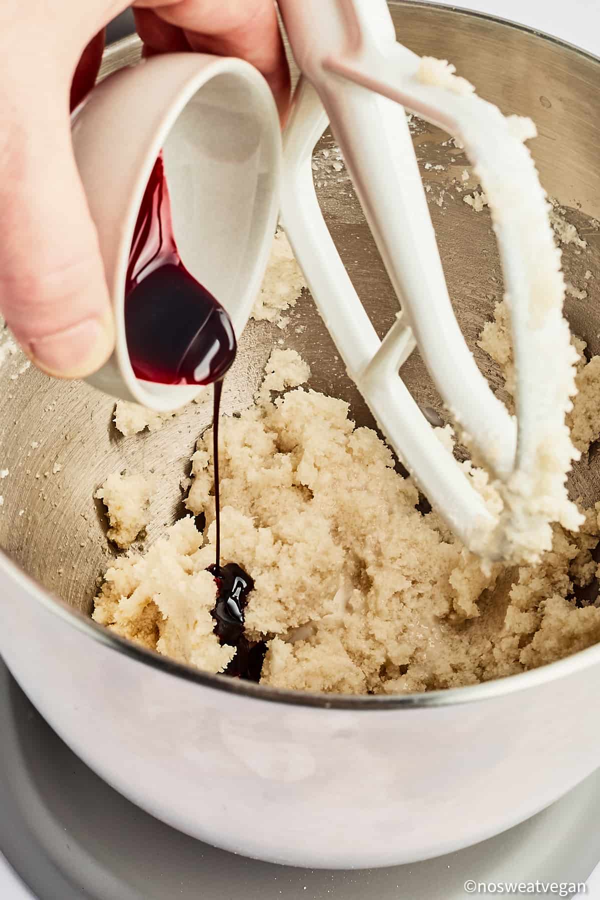 Hand adding red food coloring to vegan red velvet cookie dough.