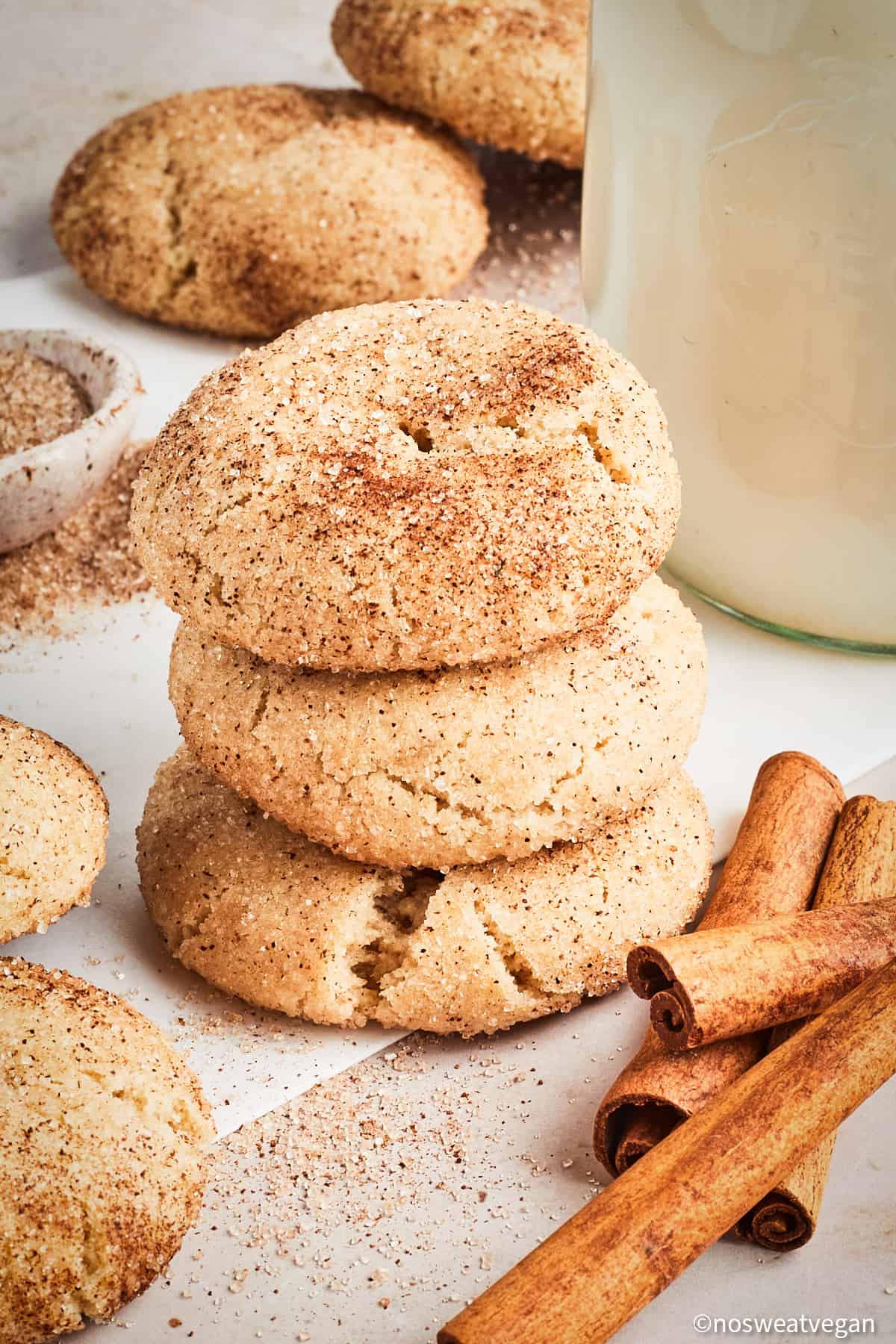 Vegan snickerdoodles stacked next to cinnamon sticks.