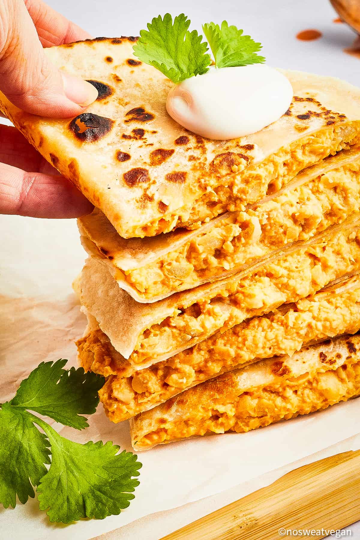 Stack of buffalo chickpea quesadilla triangles with a hand picking up the top one.