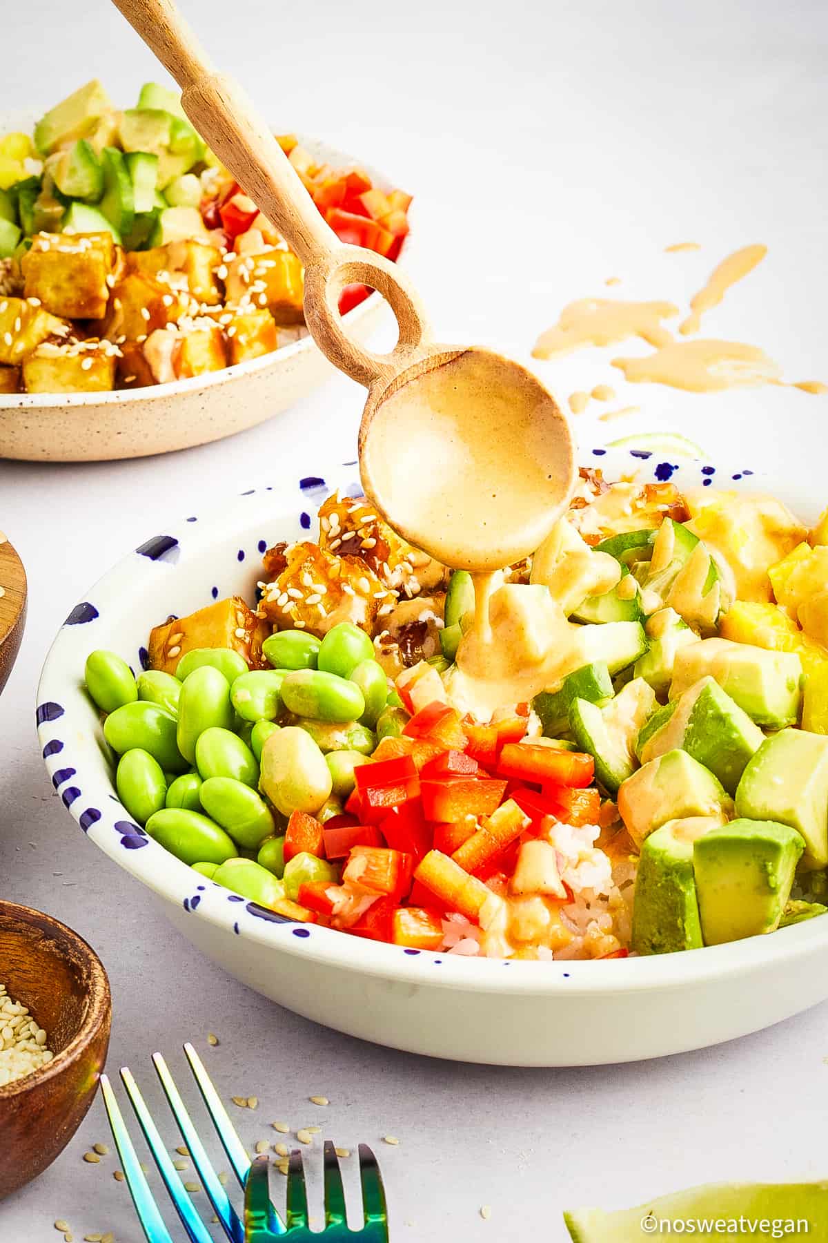 Spoon drizzling sauce over vegan poke bowl.