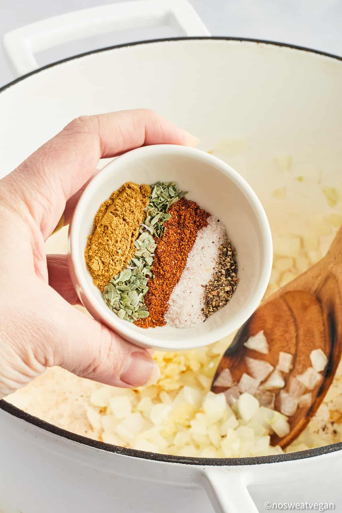 Hand adding spices to white bean chickpea chili.