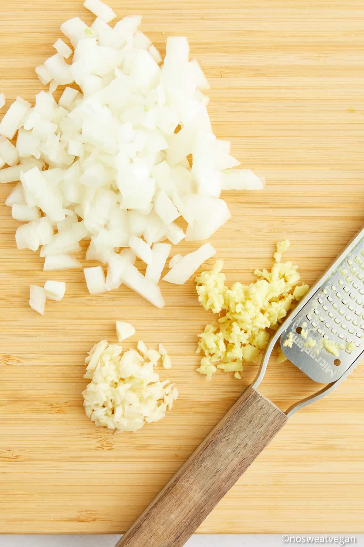 Cutting board with chopped onions, minced garlic, and ginger.