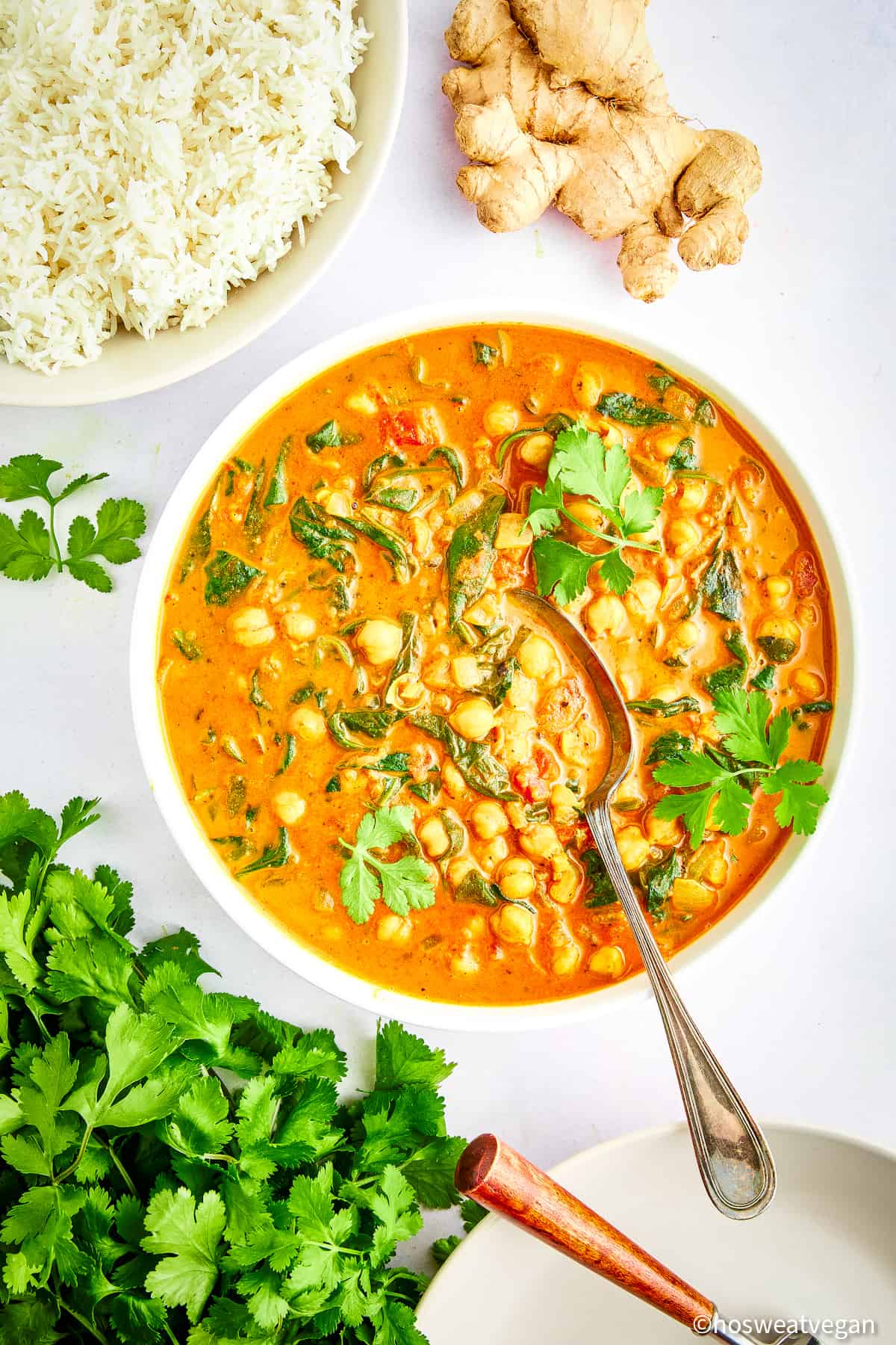 Bowl of chickpea and spinach curry next to a bowl of rice.