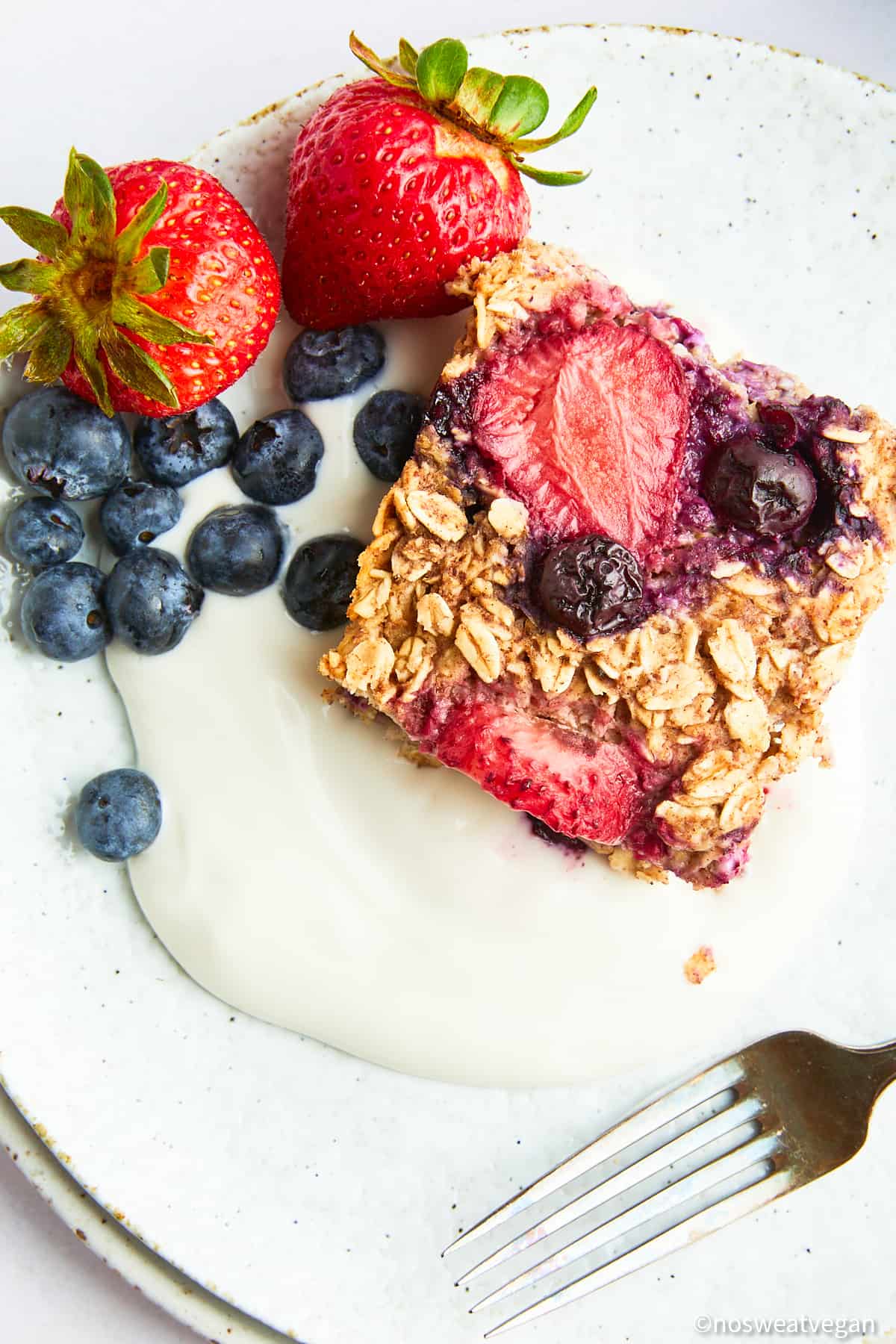 Square of vegan baked oats on a plate with yogurt and berries.