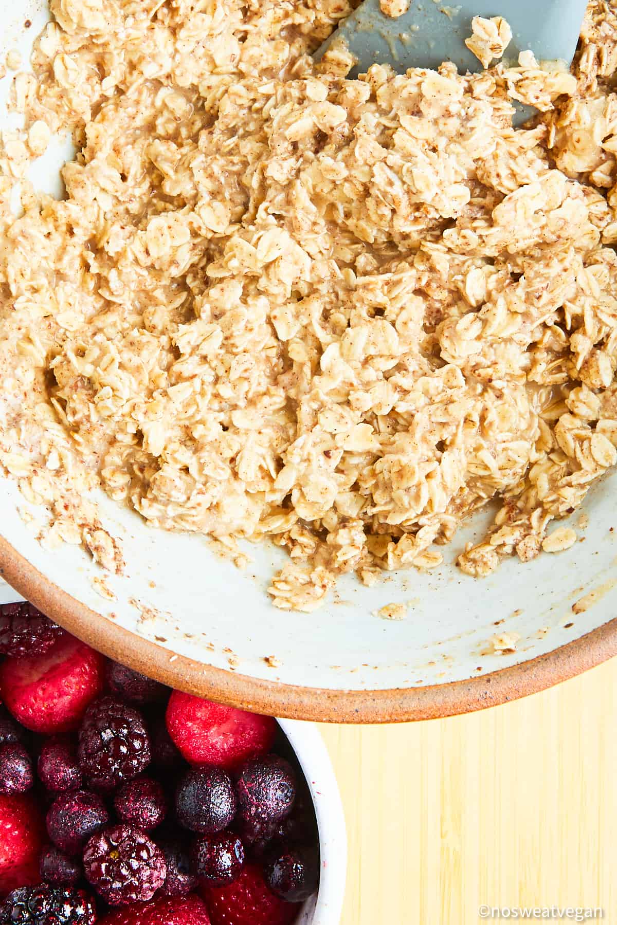 Oatmeal mixture in a bowl next to a bowl of frozen berries.