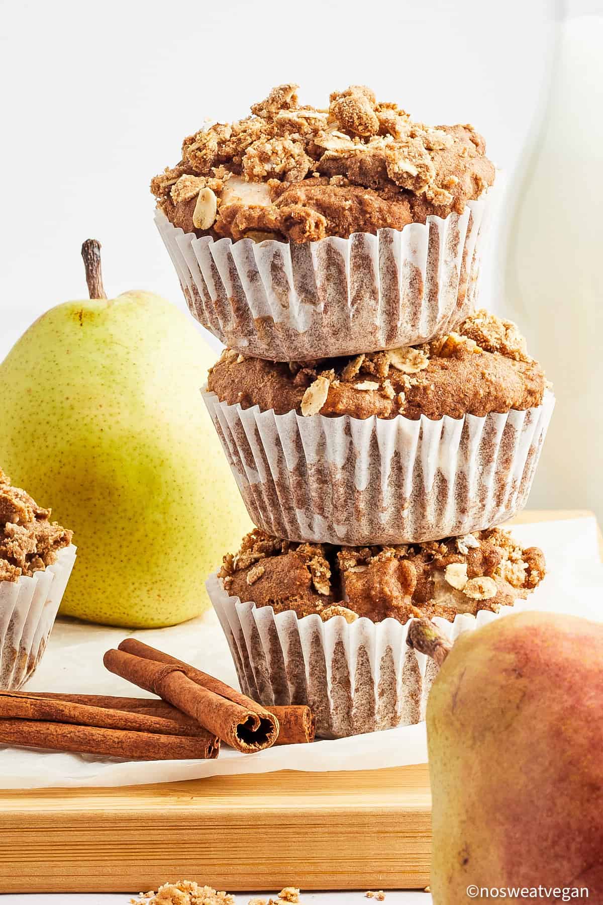 Three pear muffins stacked on a cutting board.