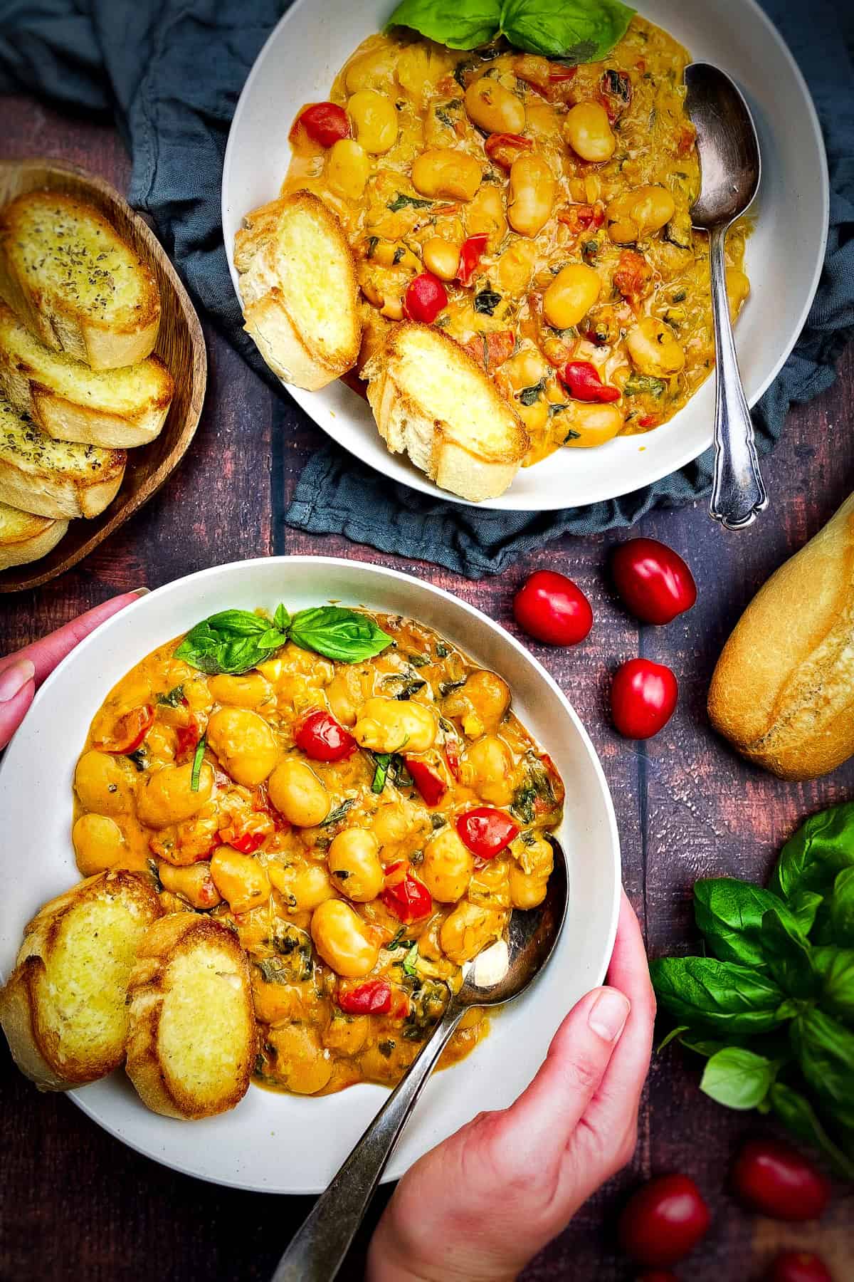 Two bowls of vegan butter beans and a plate with bread.
