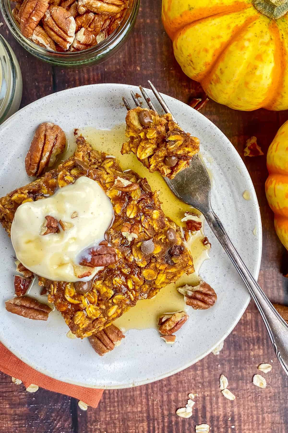 Square of vegan pumpkin baked oats on a plate topped with yogurt, maple syrup, and pecans.