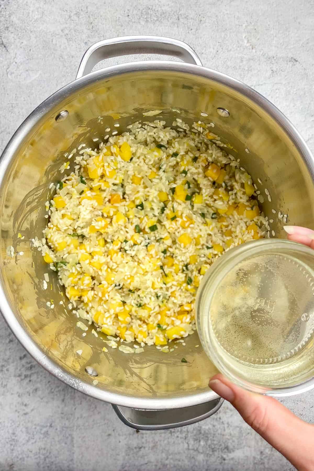 Hand adding dry white wine to risotto.