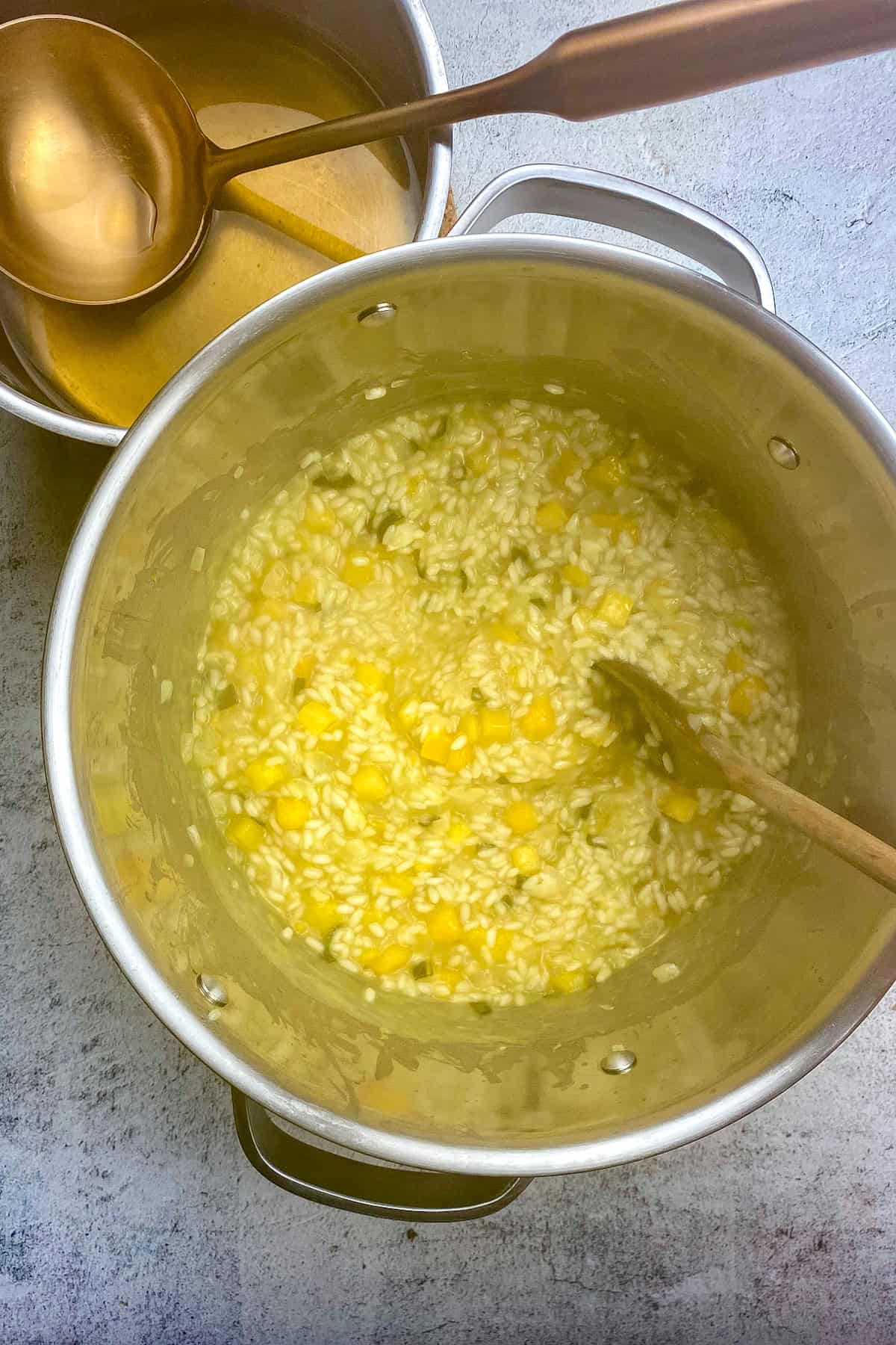 Pot of half-cooked risotto next to a smaller pot of veggie broth.