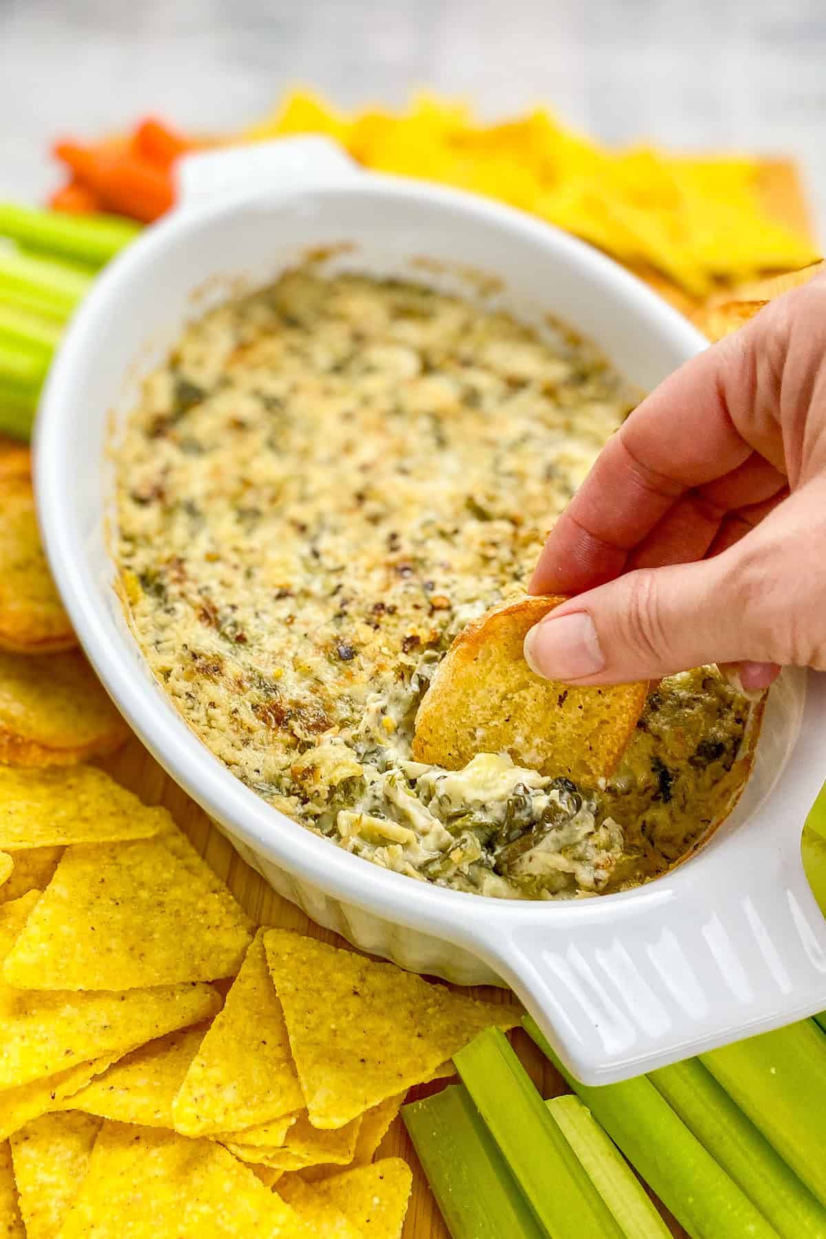 Hand dipping toast into vegan spinach artichoke dip.
