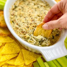 Hand dipping crostini into vegan spinach artichoke dip.