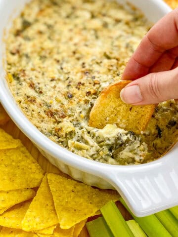 Hand dipping crostini into vegan spinach artichoke dip.
